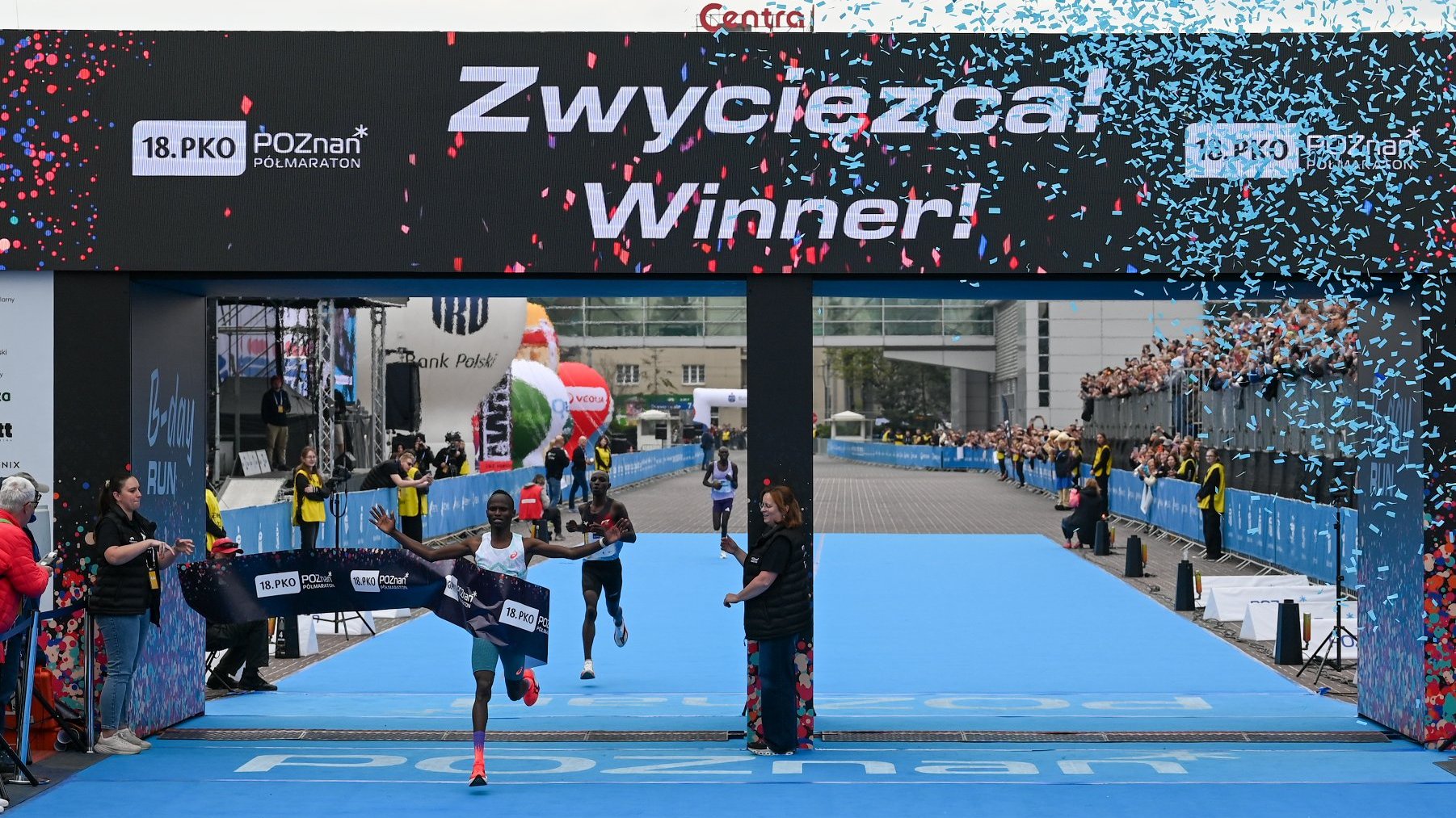 18. PKO Poznań Półmaraton - zawodnik wbiega na metę po niebieskim dywanie przy sypiącym się konfetti