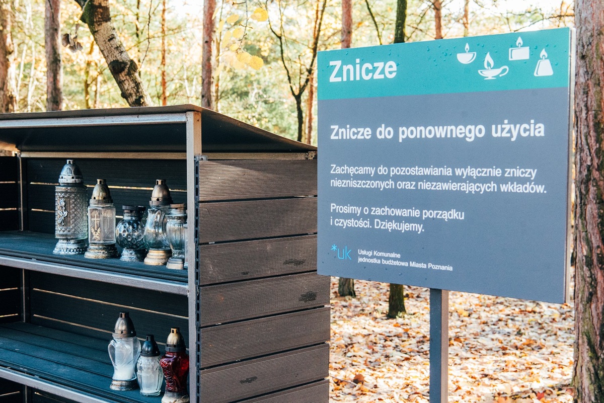 altanka na cmentarzu w niej ustawione znicze obok tablica z informacją, że są to znicze do ponownego wykorzystania