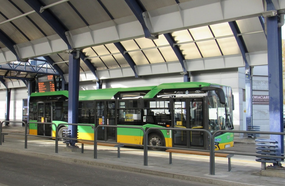 autbus komunikacji miejskiej stoi na przystnaku zadaszonym, za nim tablica świetlma z godzinami odjazdów