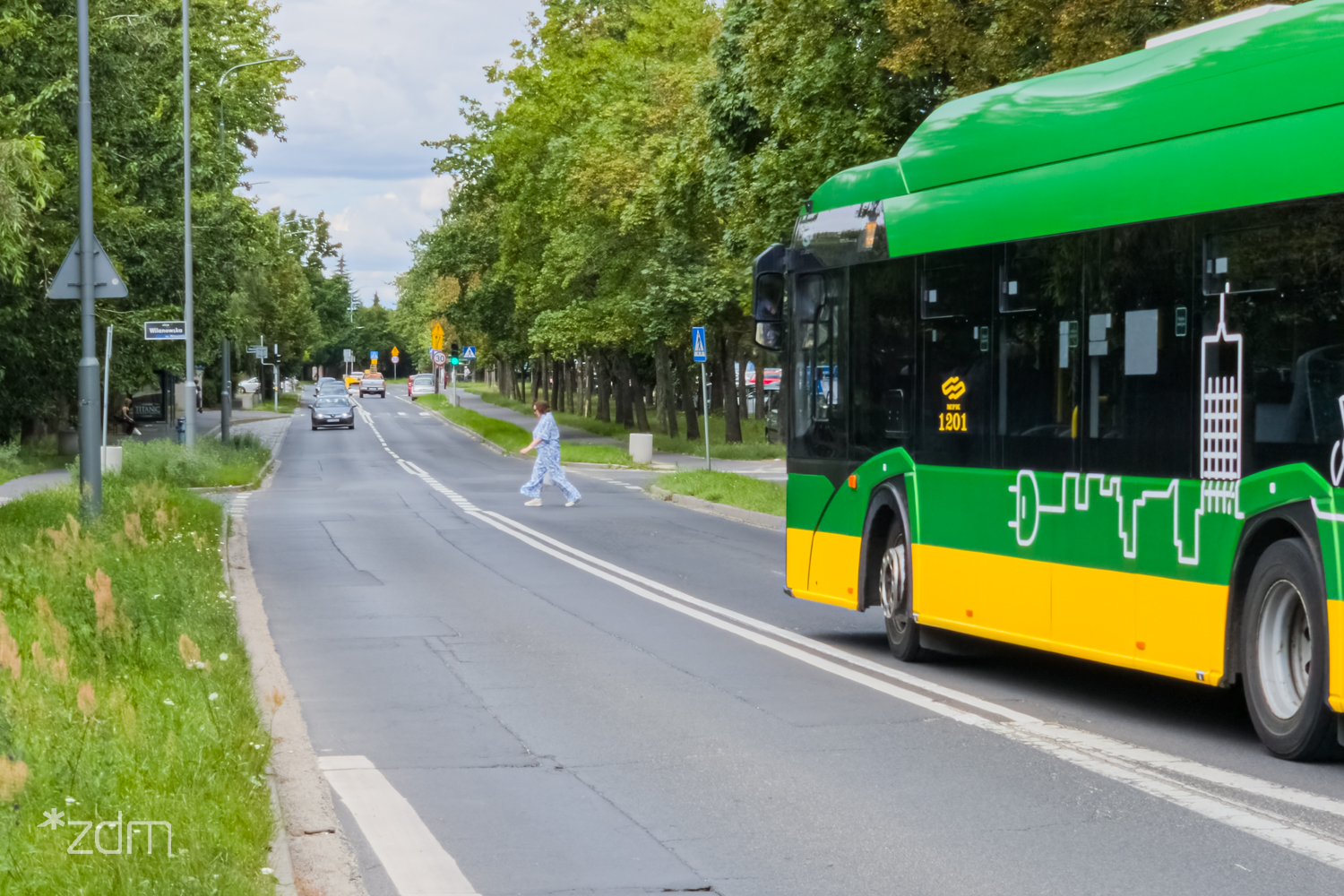 Autobus jadący ul. Stróżyńskiego. Przed nim widać osobę przechodzącą przez jezdnie