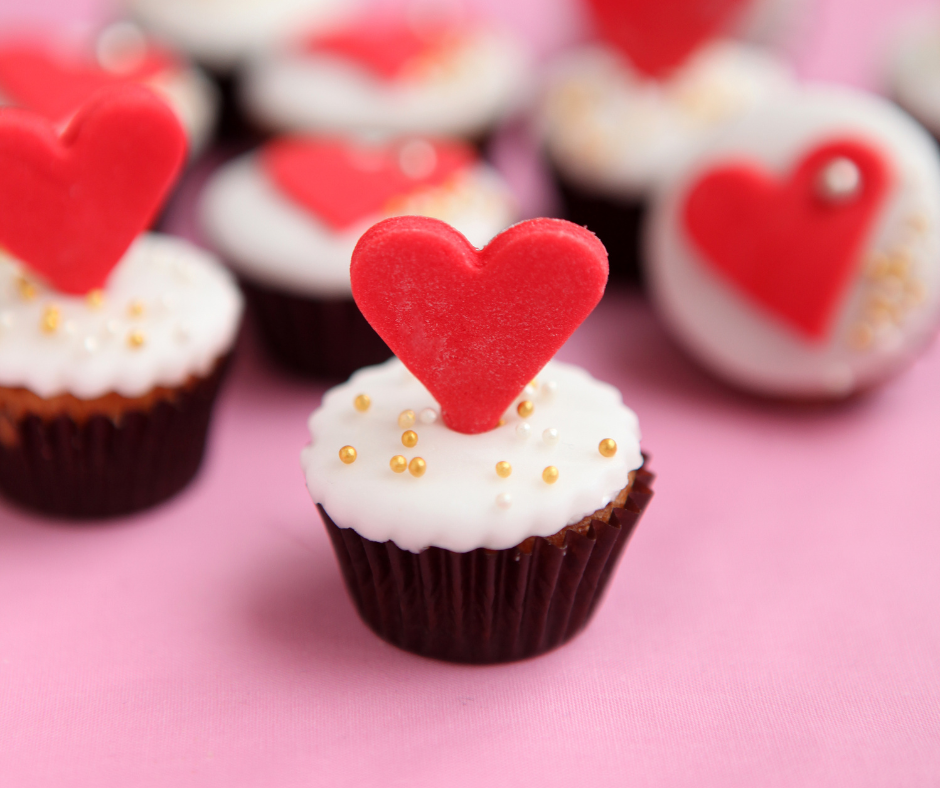 Babeczka z białym kremem, perełkową posypką i dużym czerwonym sercem.