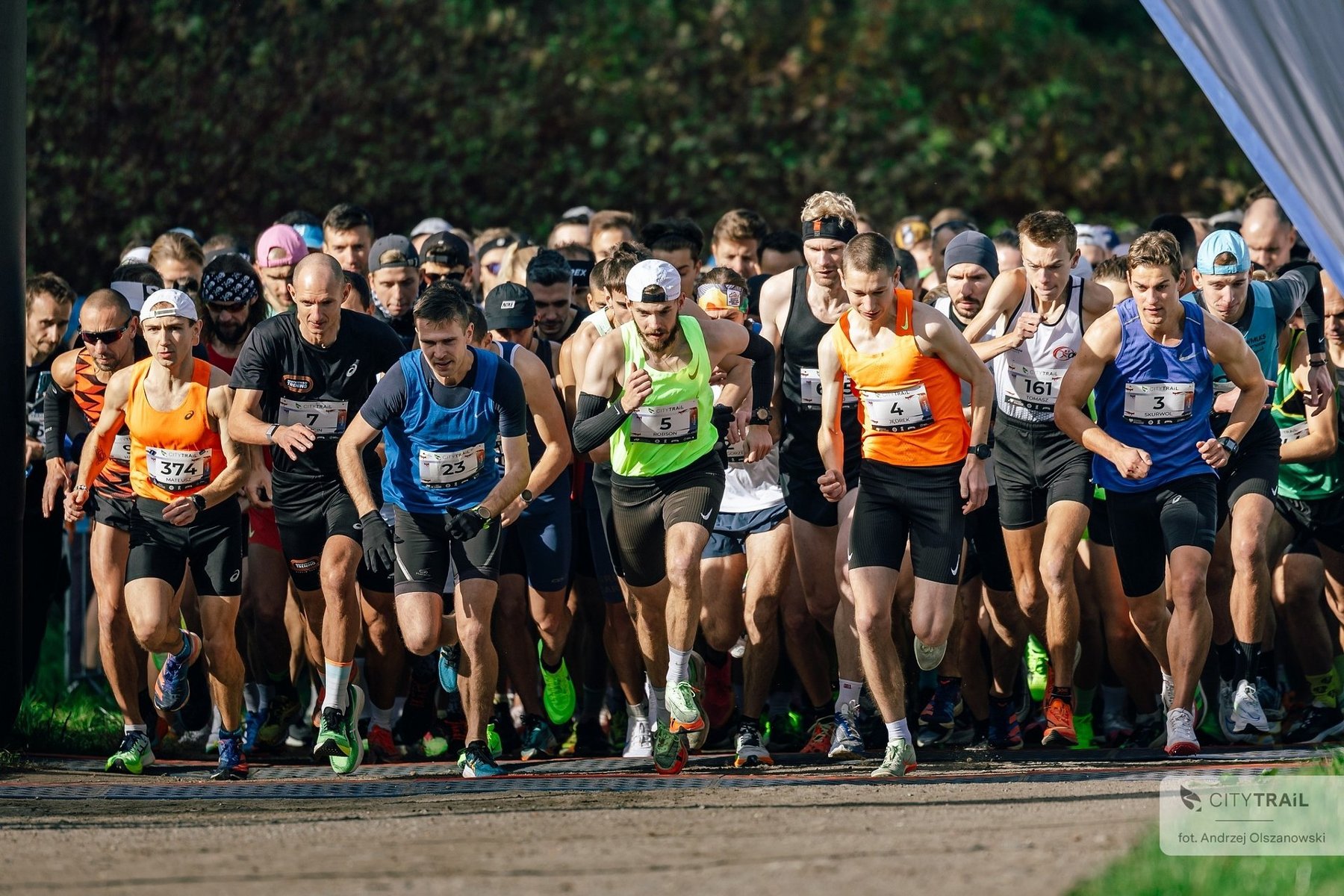Bieg City Trail, fot. Andrzej Olszanowski - tłum ludzi rozpoczyna bieg w promieniach słońca na tle terenów zielonych