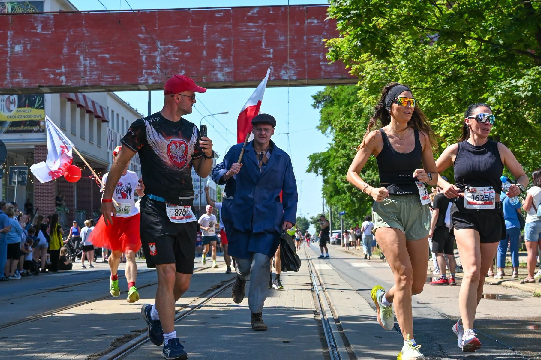Bieg Czerwca '56, fot. Facebook Bieg Czerwca '56 - zdjęcie uczestników biegu w strojach sportowych oraz jednego w stroju z epoki, trzymającego z biało-czerwoną flagą