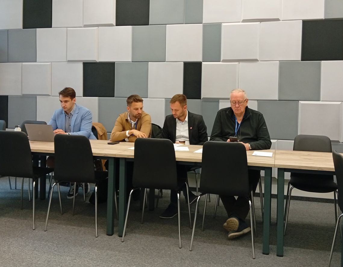 czterech mężczyzn siedzi za stołem w sali konferencyjnej - grafika artykułu