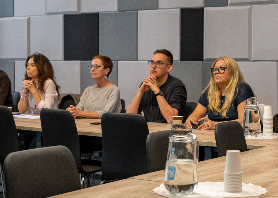 cztery osoby siedzą w sali przy stole konferencyjnym, patrzą w jedną stronę - grafika artykułu