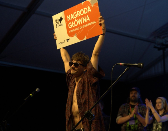 Dawid Tysowski podnoszący do góry tablicę z informacją o wygraniu Go On Stage Festival