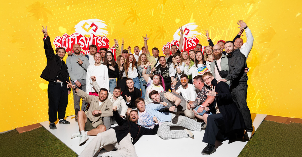 Duża grupa ludzi pozuje na tle żółtej ścianki. Ludzie są uśmiechnięci, cieszą się.