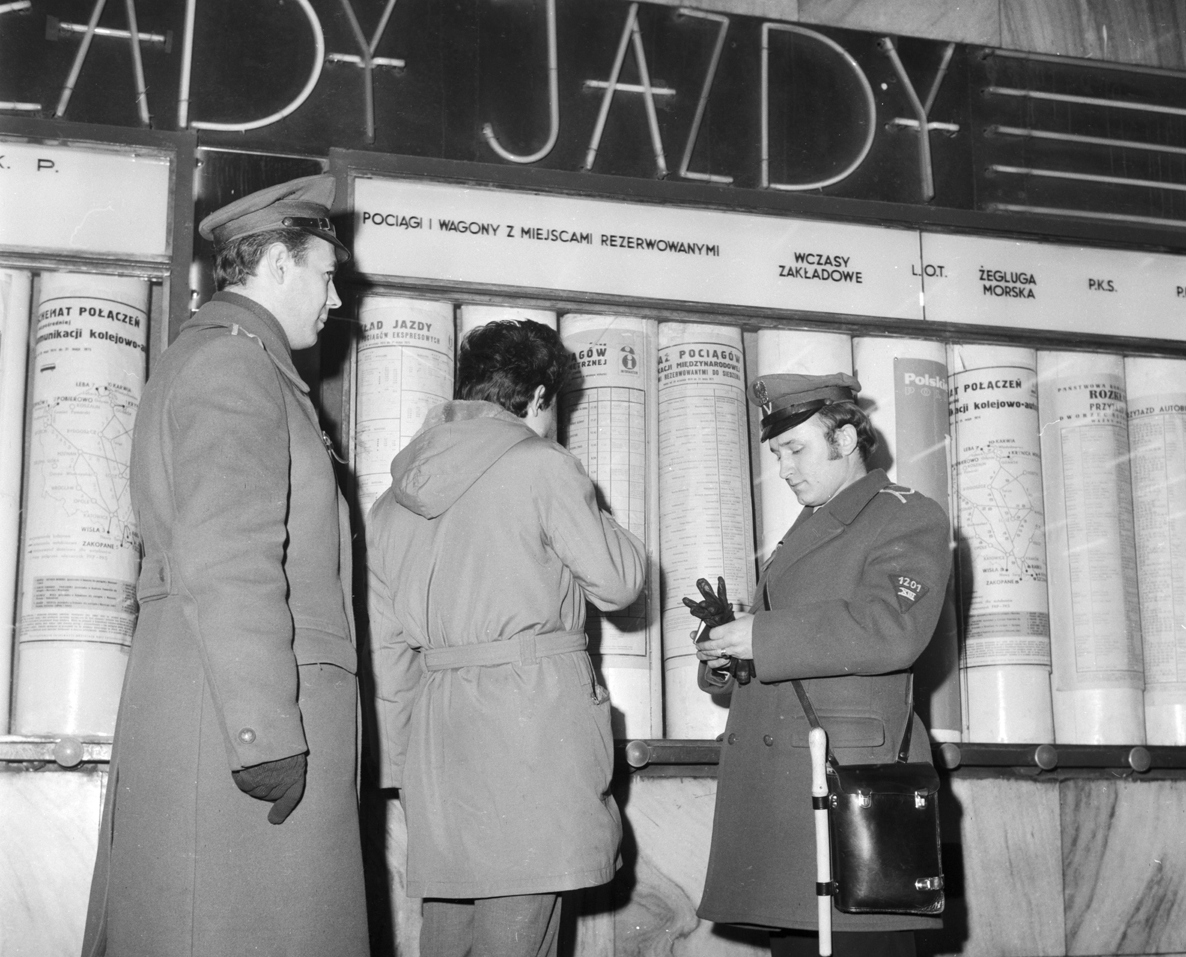 Dwaj milicjanci, w mundurach z lat 70, przeglądają dokumenty mężczyzny