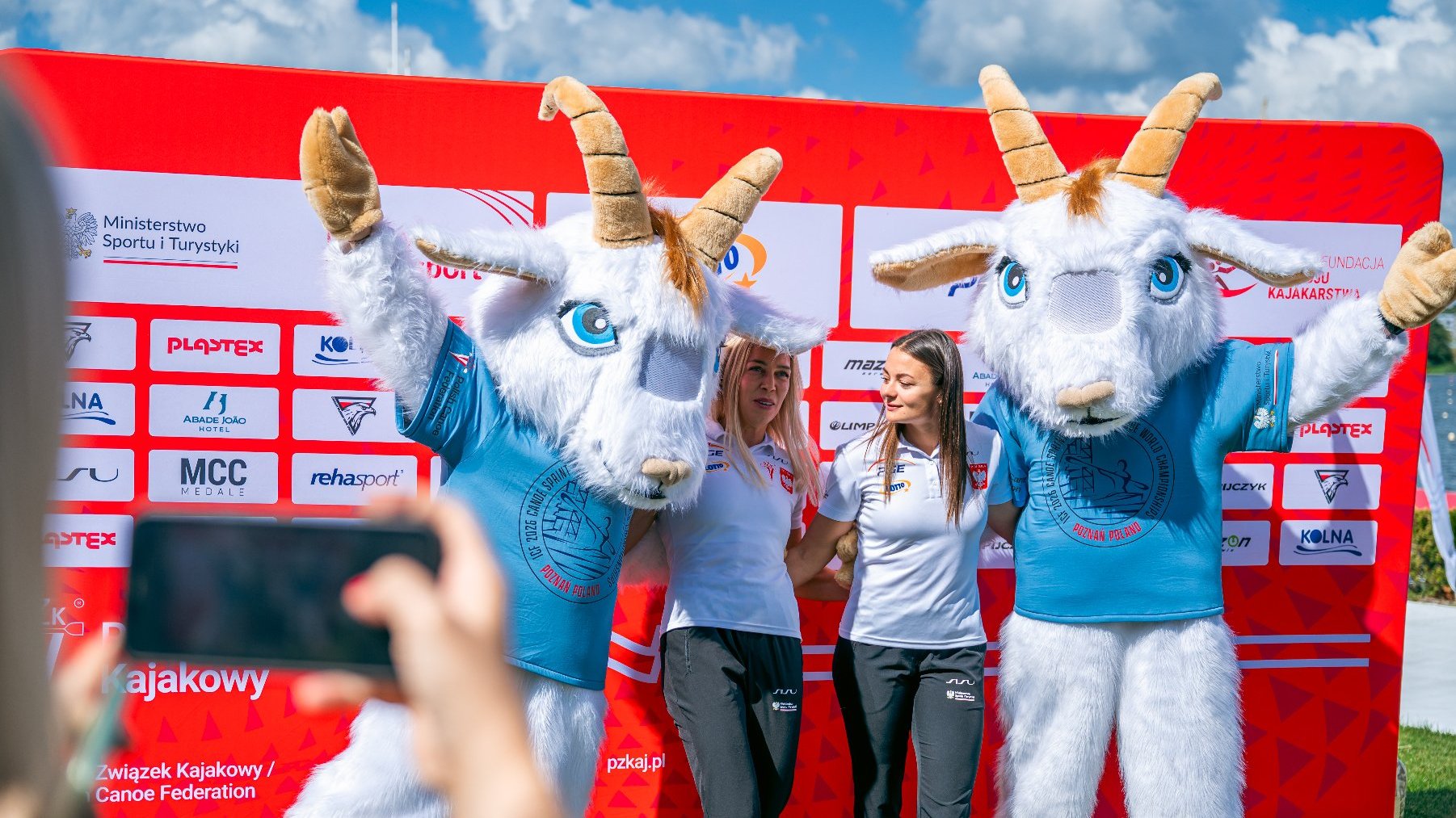 Dwie osoby przebrane za koziołki poznańskie. Pozują do zdjęcia z dwoma sportowczyniami.