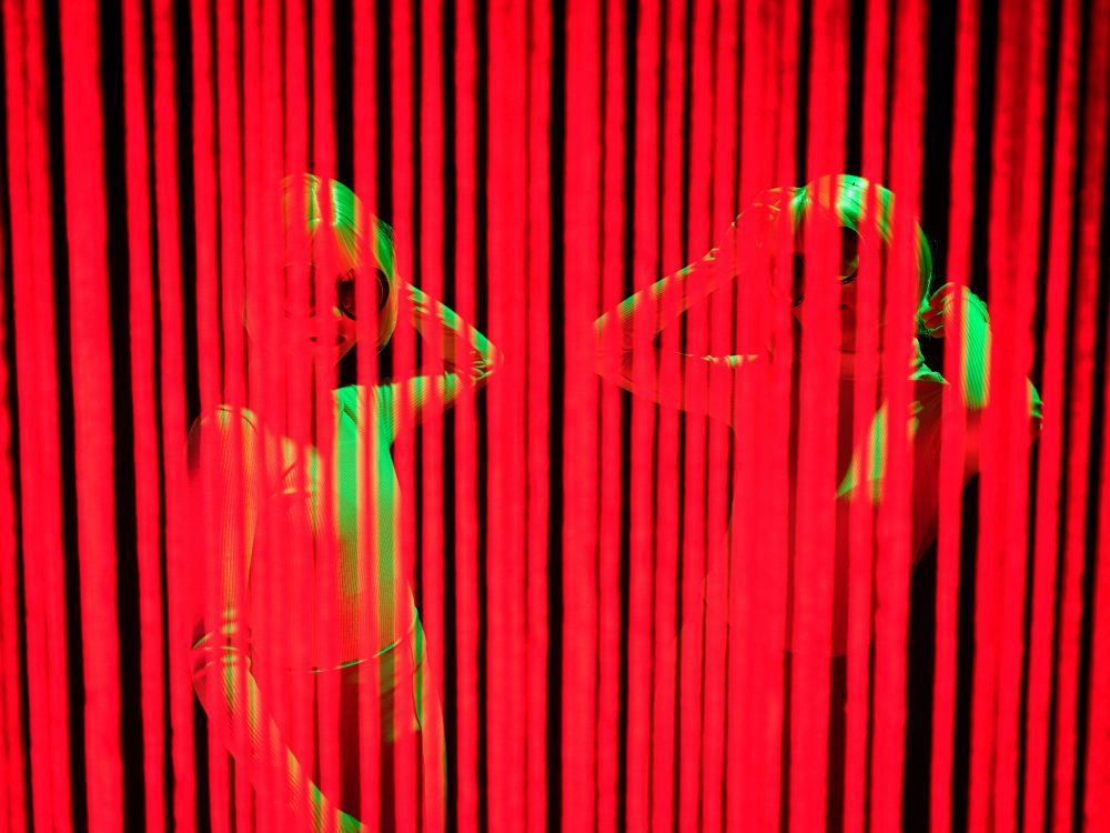 Dwie postaci kobiece za zasłoną z czerwonych pasków.