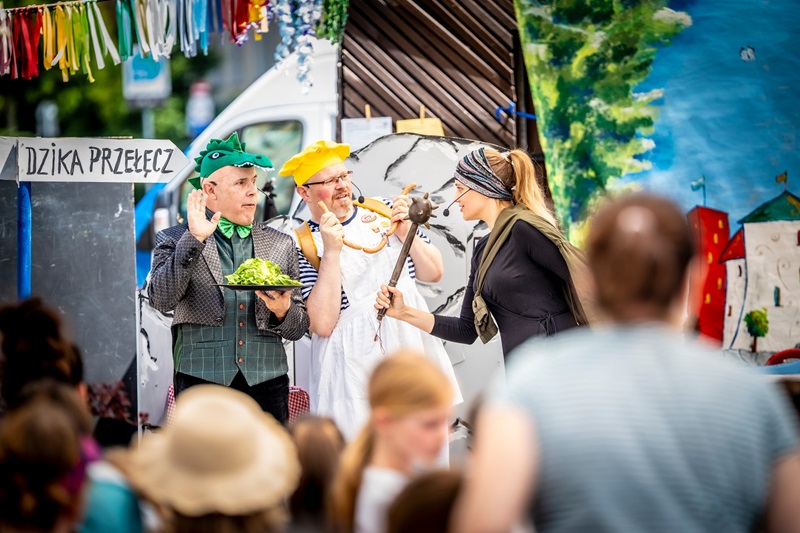Dwóch mężczyzn po lewej - przebrani za krokodyla i kucharza. Po prawej kobieta, trzyma w ręku maczugą. Są to aktorzy w trakcie przedstawienia dla dzieci. Po prawej stronie napis na tabliczce - dzika przełęcz.