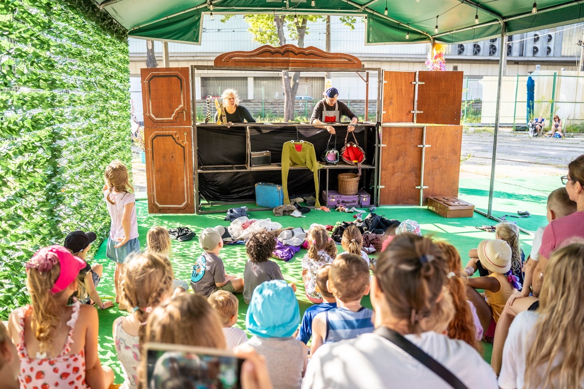 Dwójka aktorów występuje przed dziećmi. Stoją oni za rozkładanym drewniany prarawanem. Na jego tle odgrywają przedstawienie.