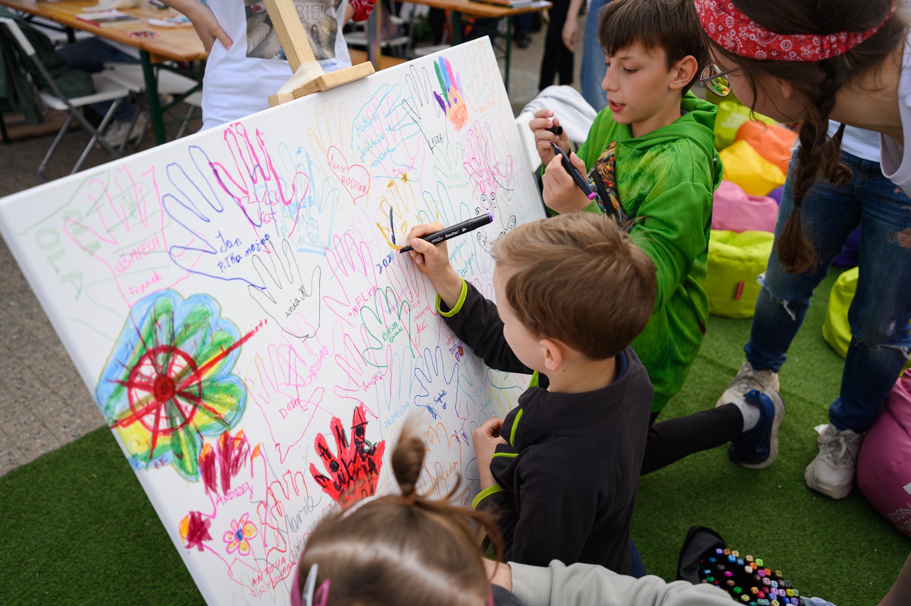 dzieci rysujące na białej tablicy, a na niej odciski dziecięcych rączek