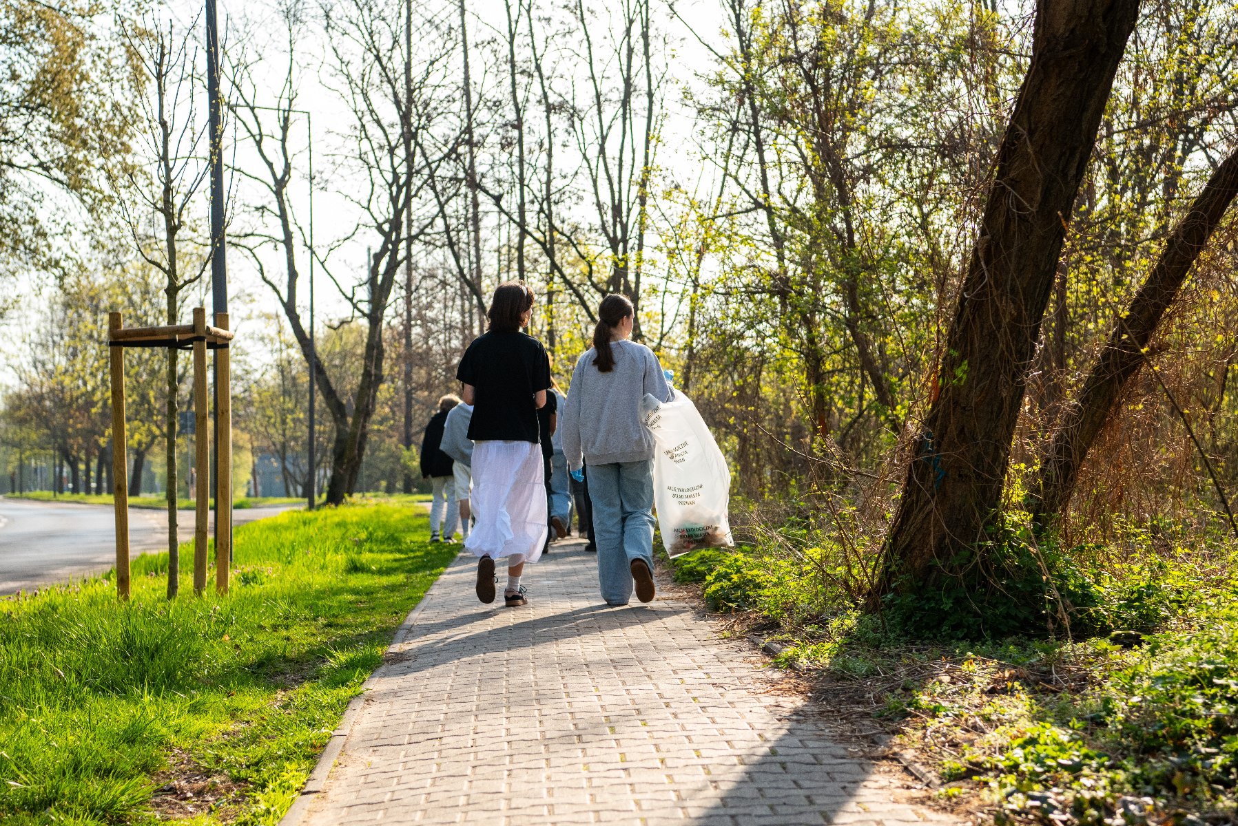 Dziwwczyny idące chodnikiem, trzymające worki ze śmieciami - uczestniczą w akcji "Sprzątanie świata"