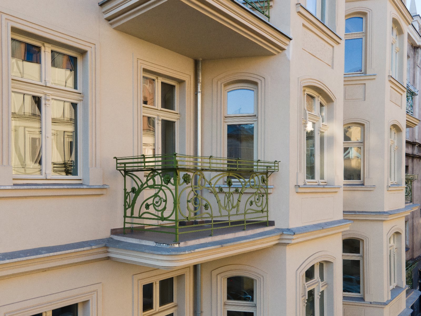 Fragment odnowionej elewacji zabytkowej kamienicy z ozdobnym, zielonym balkonem i secesyjną balustradą.
