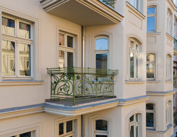 Fragment odnowionej elewacji zabytkowej kamienicy z ozdobnym, zielonym balkonem i secesyjną balustradą.