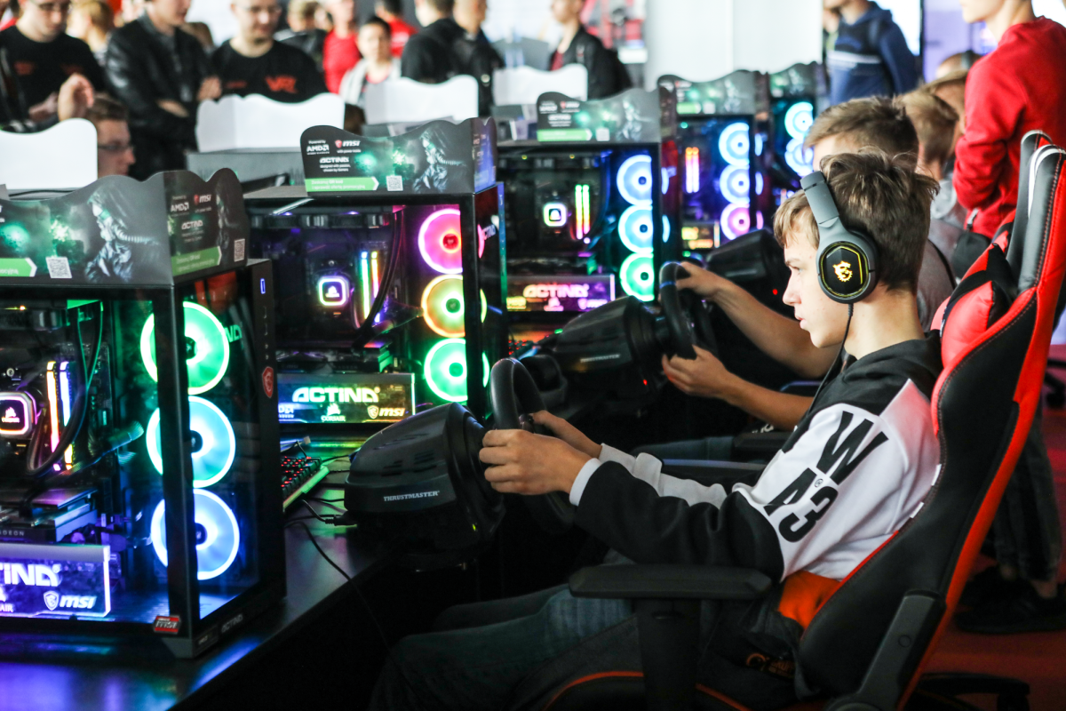 Głównie młodzi ludzie siedzący prze komputerami gamingowymi