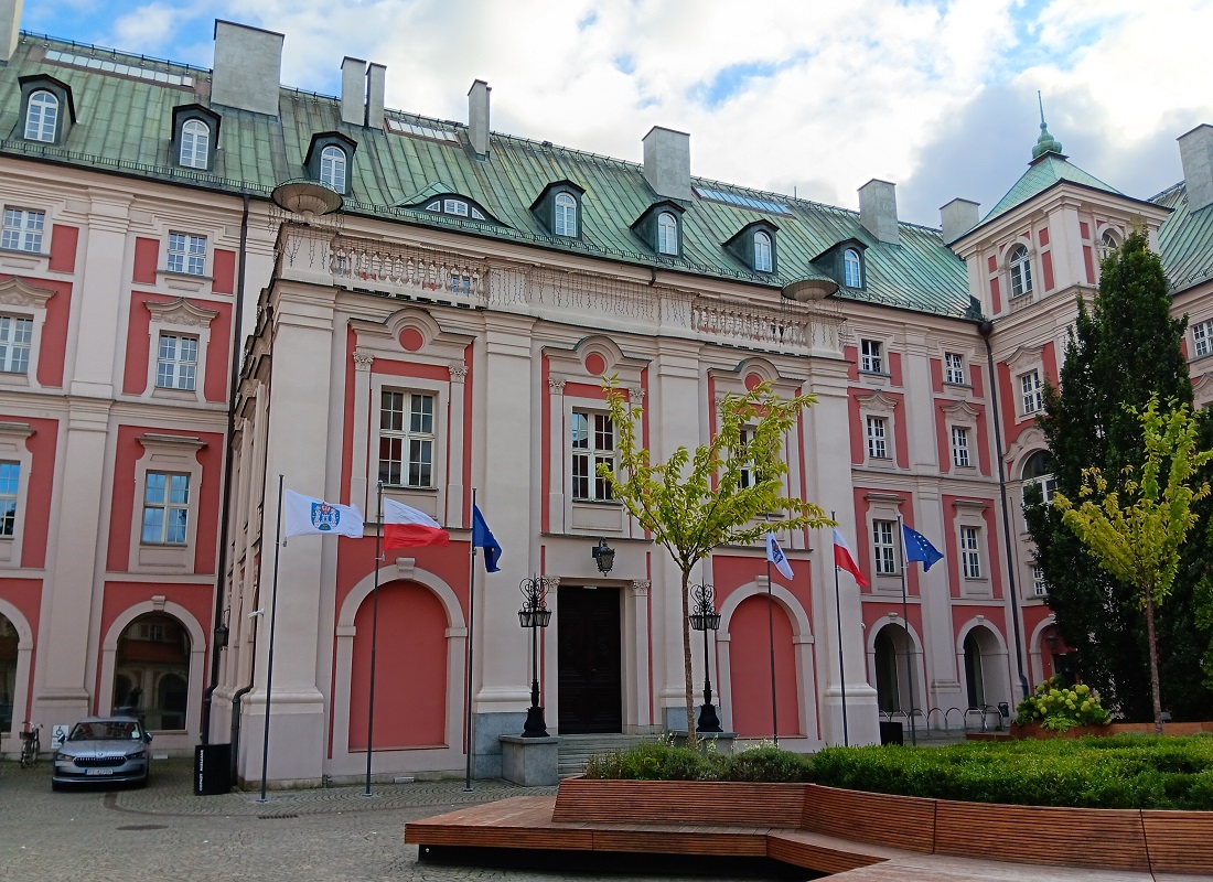 gmach Urzędu Miasta Poznania od strony dziedzińca zabytkowa architektura przed wejście do gmachu ławki i zieleń oraz flagi na masztach flaga Poznania Polski i Unii Europejskiej