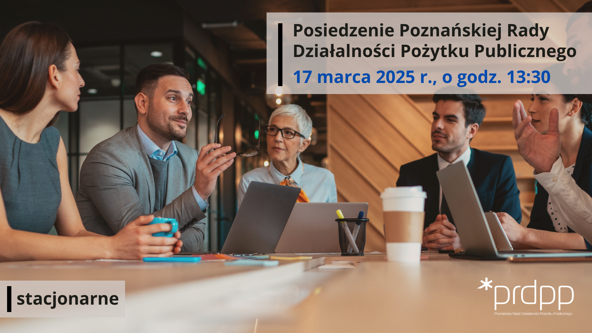 grafika przedstawia osoby siedzące przy stole z otwartymi laptopami i dokumentami, dyskutujące