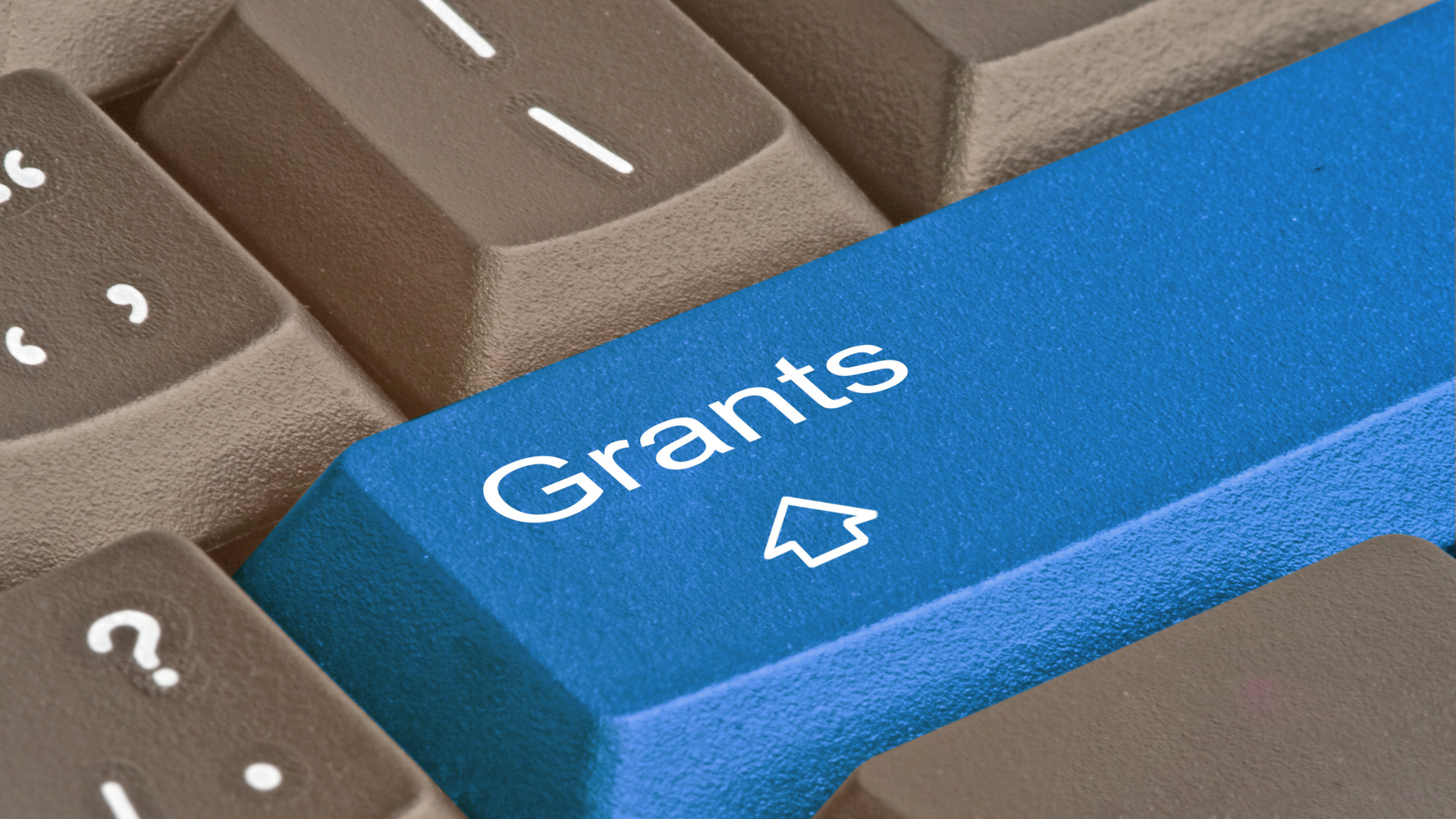 grafika przedstawia szarą klawiaturę komputera w przybliżeniu na kilka klawiszy, w tym klawisz shift, w kolorze niebieskim, z napisem "grants" zamiast "shift"