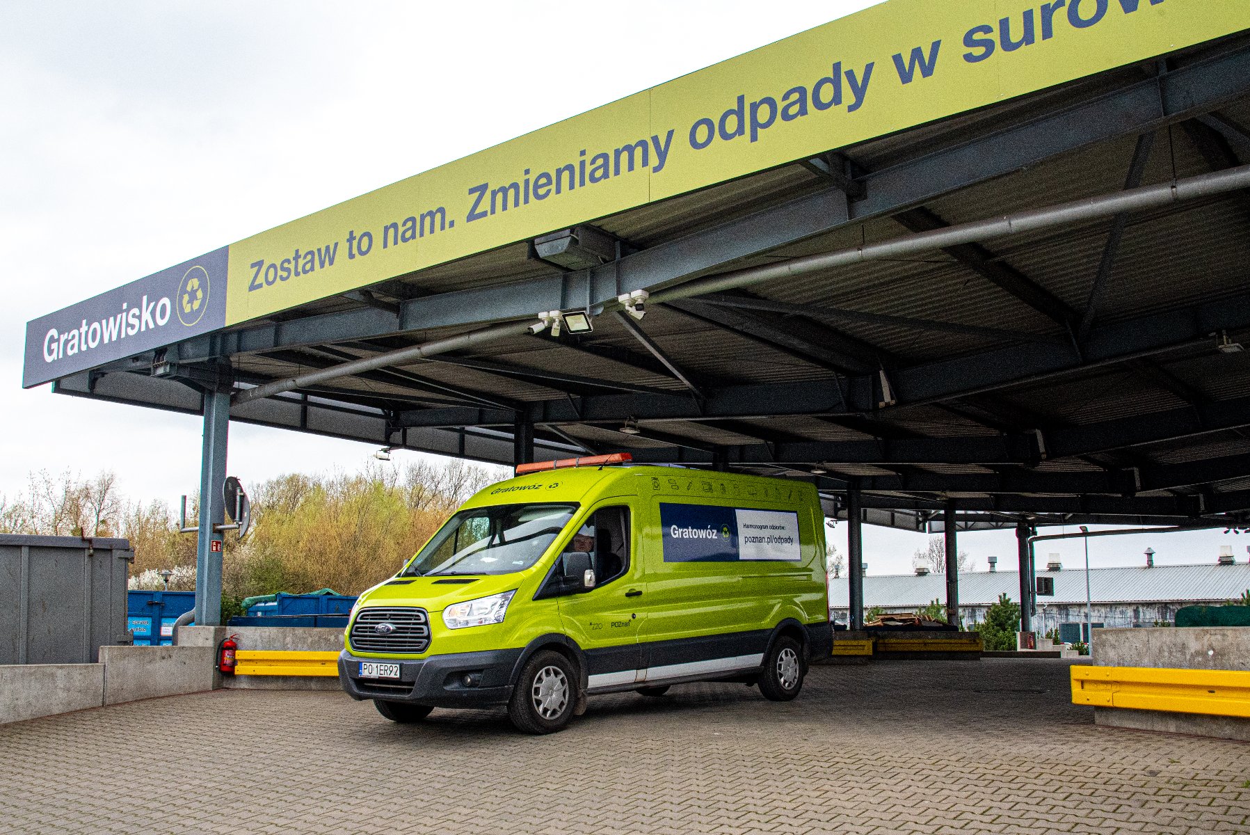 Grafika przedstawia żółty pojazd "gratowóz" ustawiony pod wiatą gratowiska