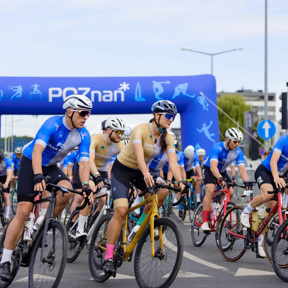 Gran Fondo Poznań 2025, fot. Facebook Gran Fondo - zawodnicy jadą na rowerze. W tle widać bramę z logotypem Poznania ora bloki