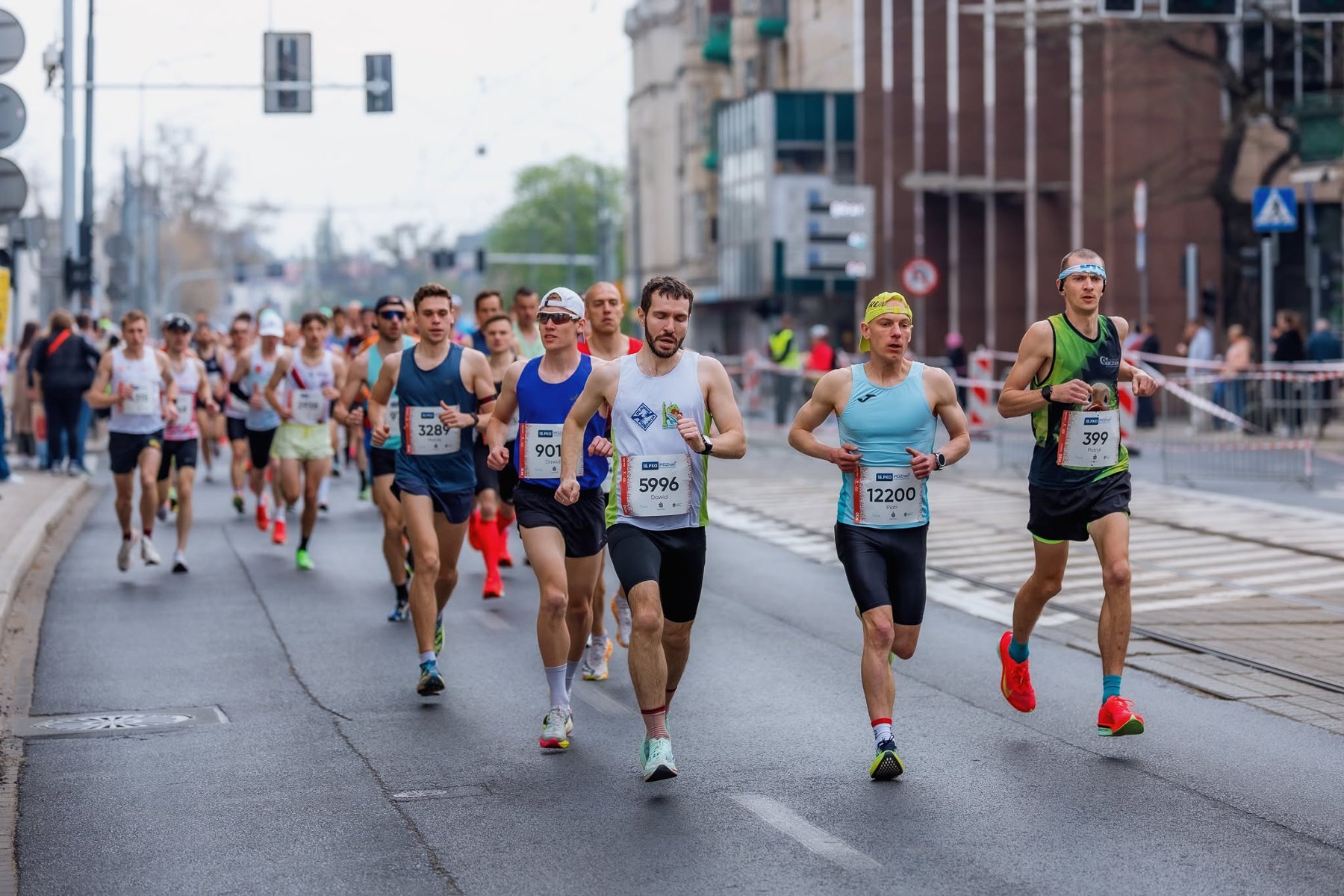 Grupa biegaczy w trakcie Poznań Maratonu, rywalizująca na wyłączonej z ruchu ulicy miejskiej.