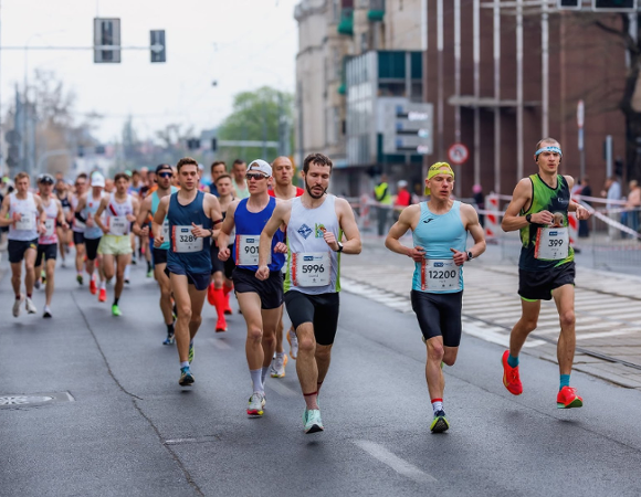Grupa biegaczy w trakcie Poznań Maratonu, rywalizująca na wyłączonej z ruchu ulicy miejskiej.