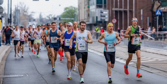 Grupa biegaczy w trakcie Poznań Maratonu, rywalizująca na wyłączonej z ruchu ulicy miejskiej.