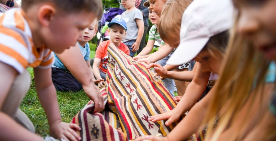 Grupa dzieci bawi się na trawie rozwijając kolorowy dywan.
