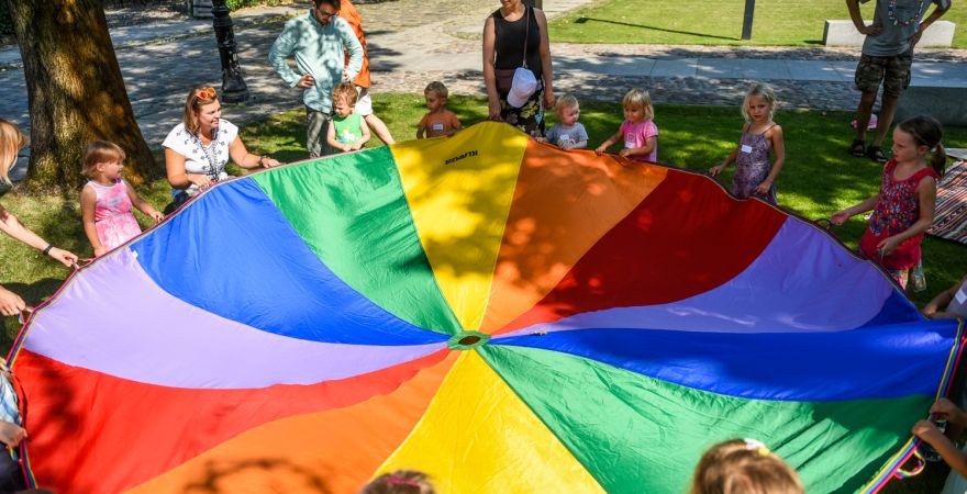 Grupa dzieci bawi się w parku kolorową chustą.