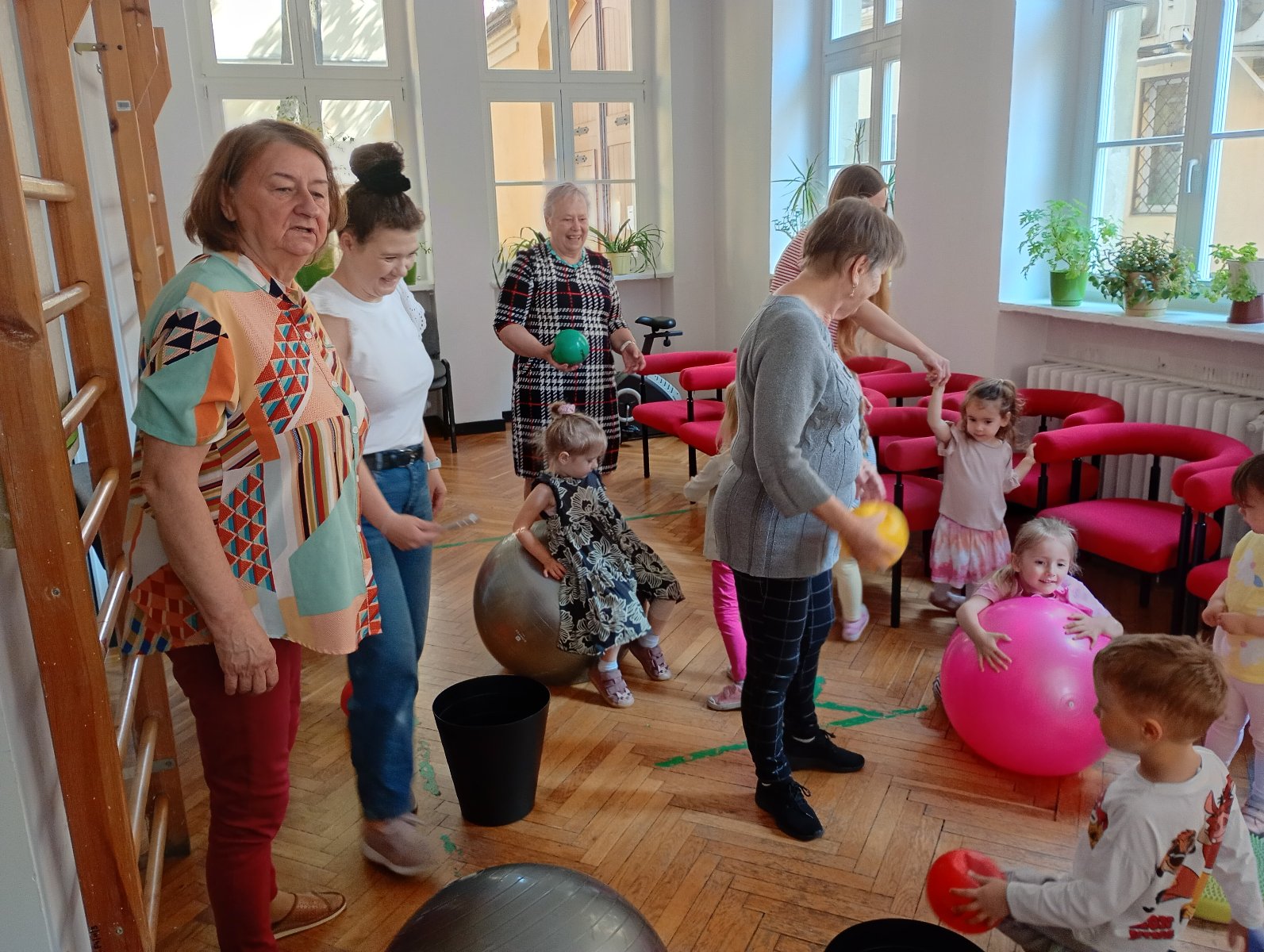 Grupa dzieci oraz dorosłych wspólnie bawią się mniejszymi i większymi piłkami