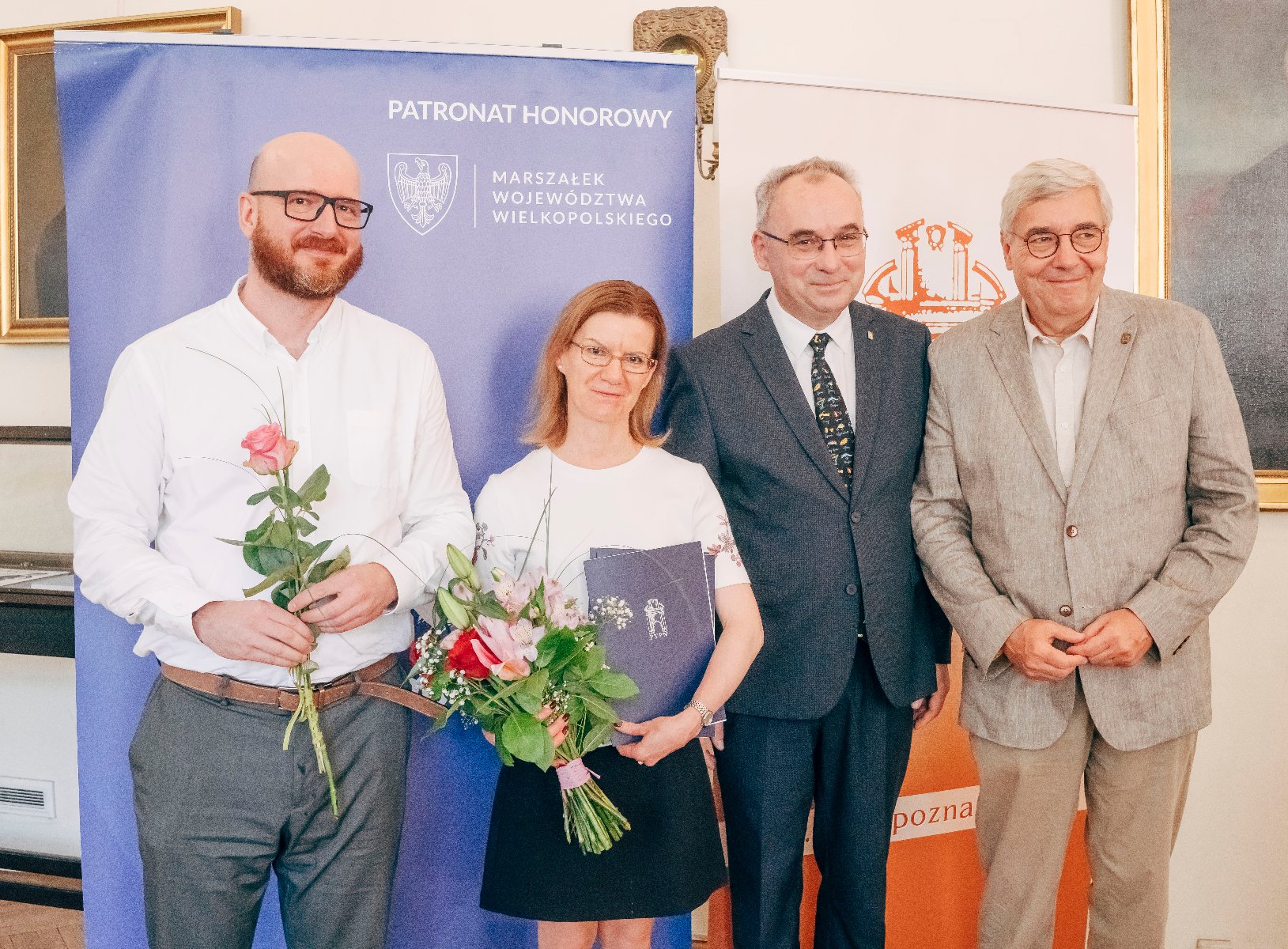 Grupa ludzi pozuje do zdjęcia z dyplomami i kwiatami.