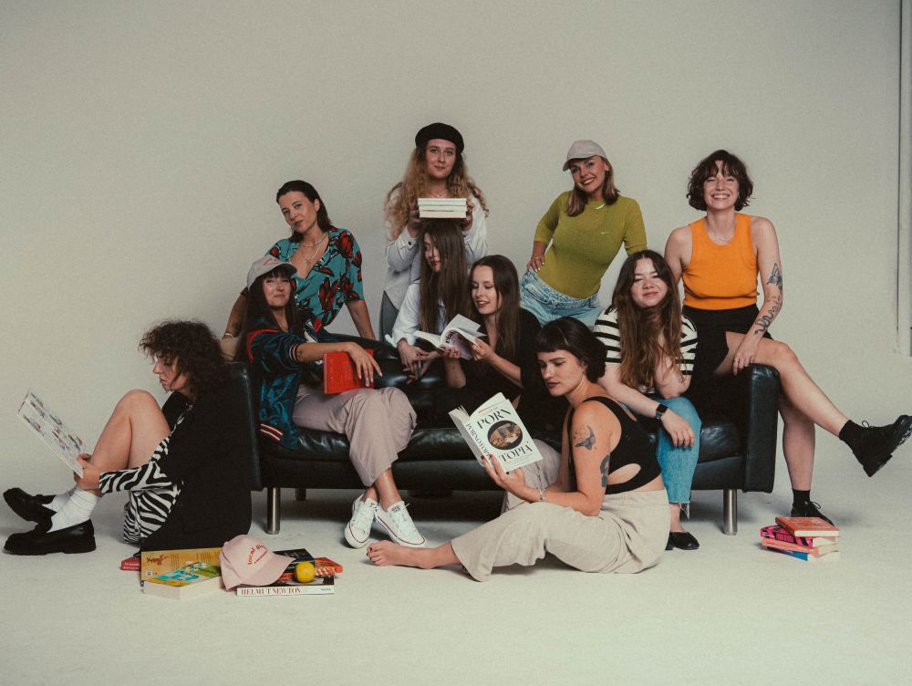 Grupa młodych kobiet pozuje do zdjęcia siedząc na i obok czarnej kanapy i czytając książki.