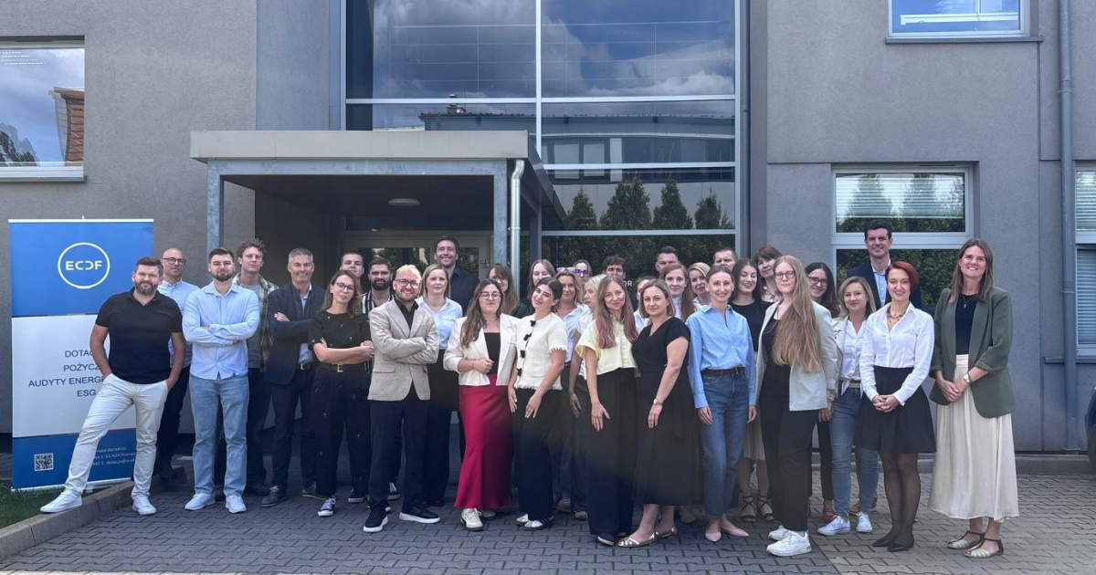 Grupa ok. 30 osób pozuje razem przed wejściem do budynku.