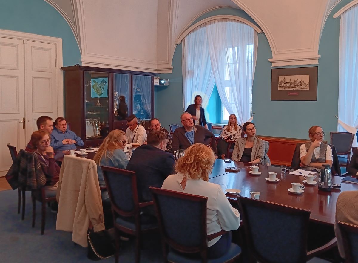 grupa około kilkunastu osób obraduje w długim stole konferencyjnym, zwróceni są wszyscy w jedną stronę - więcej w treści artykułu