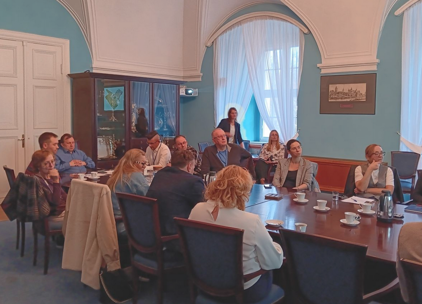 grupa około kilkunastu osób obraduje w długim stole konferencyjnym, zwróceni są wszyscy w jedną stronę - więcej w treści artykułu - grafika artykułu