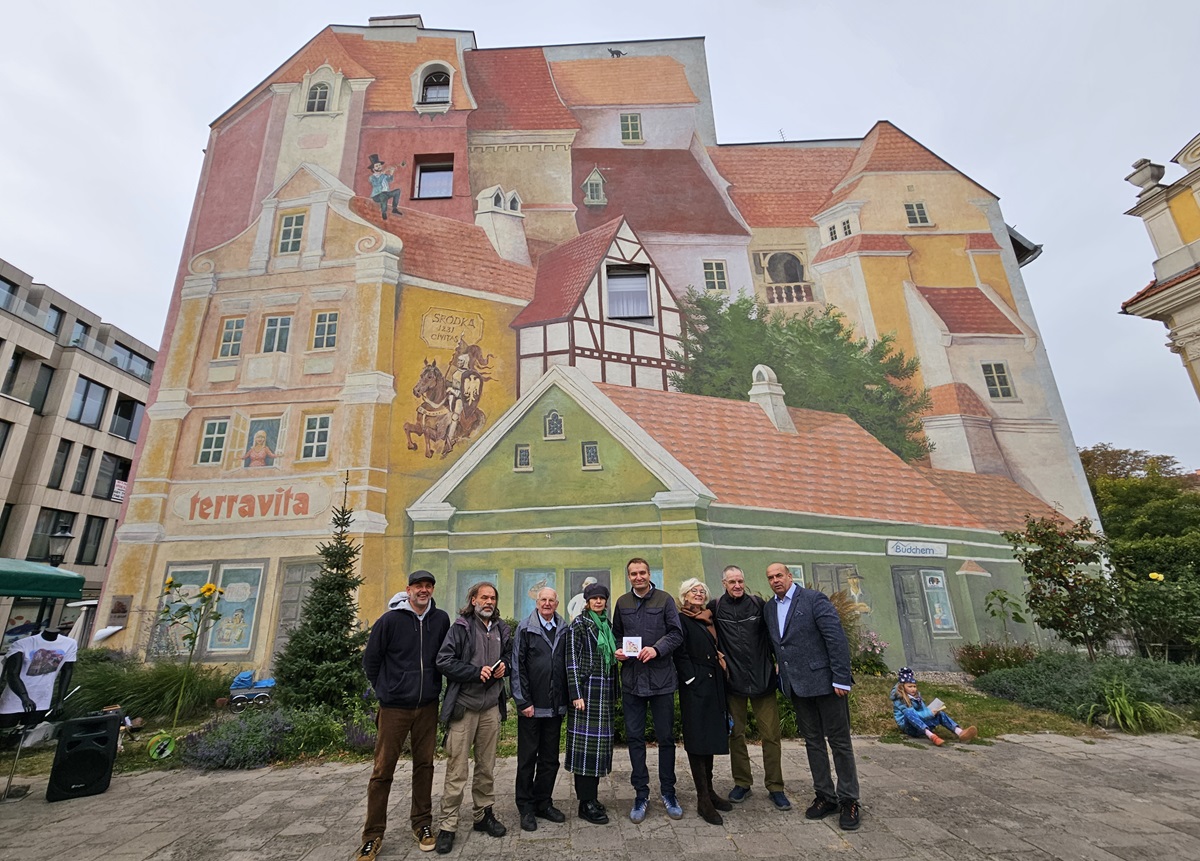 Grupa osób na pamiątkowym zdjęciu na tle muralu śródeckiego.