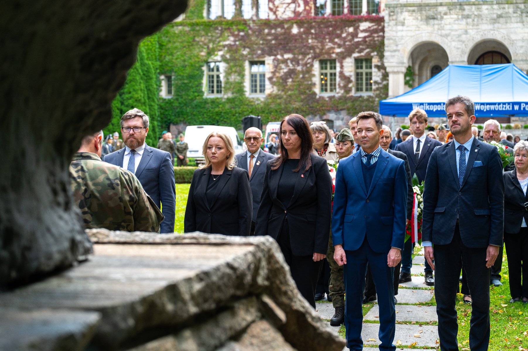 Grupa osób oddaje hołd przed pomnikiem.