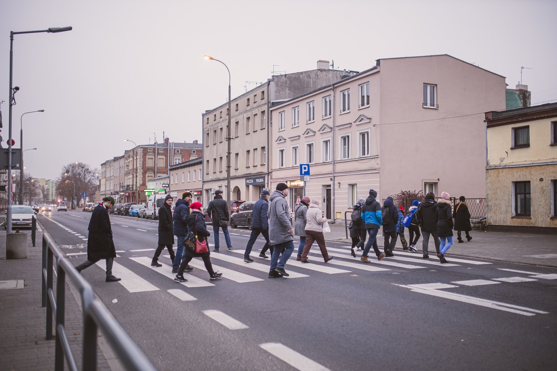 grupa osób przechodzi po pasach przez jezdnię, wzdłuż ulicy stoją dwu i trzy kondygnacyjne kamienice