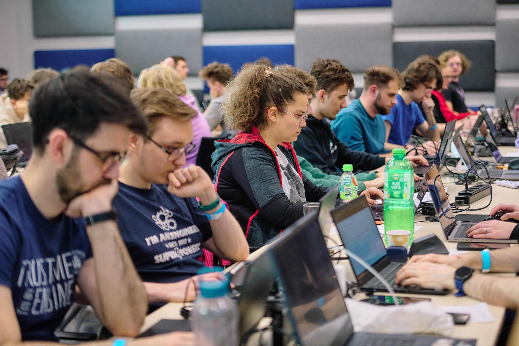 Grupa osób siedzi przy komputerach. Programują w zamyśleniu.