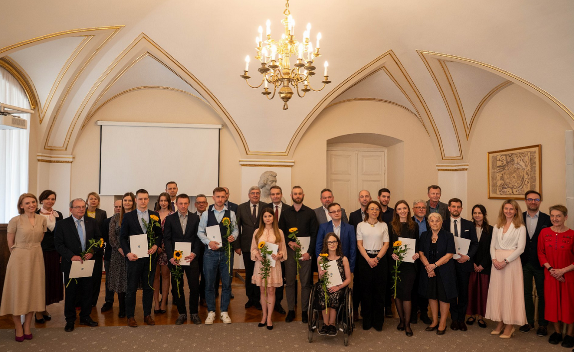 Grupa osób stoi w eleganckim wnętrzu, prawdopodobnie podczas ceremonii wręczenia nagród.