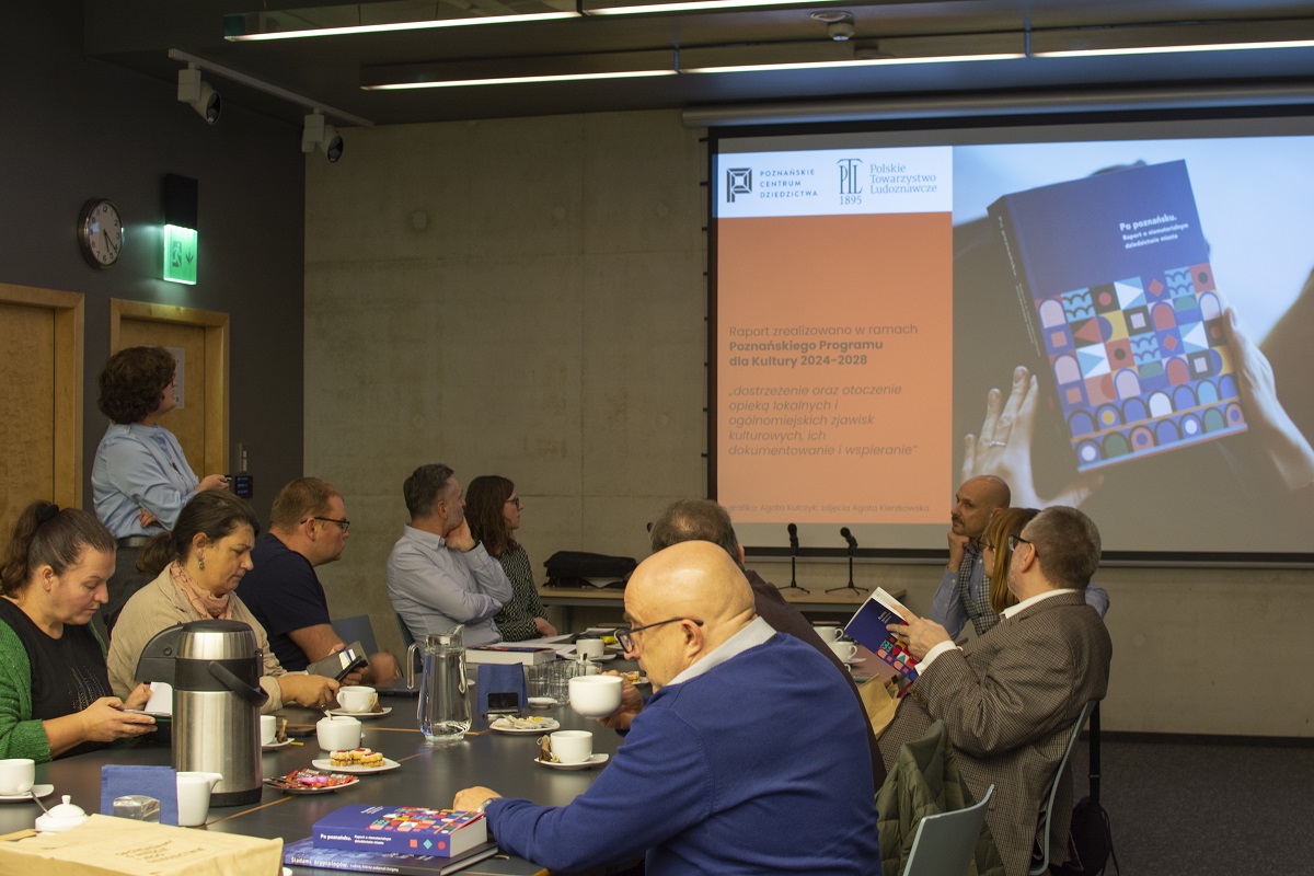 grupa osób w sali konferencyjnej siedzi przy stole i ogląda prezentację multimedialną na ekranie