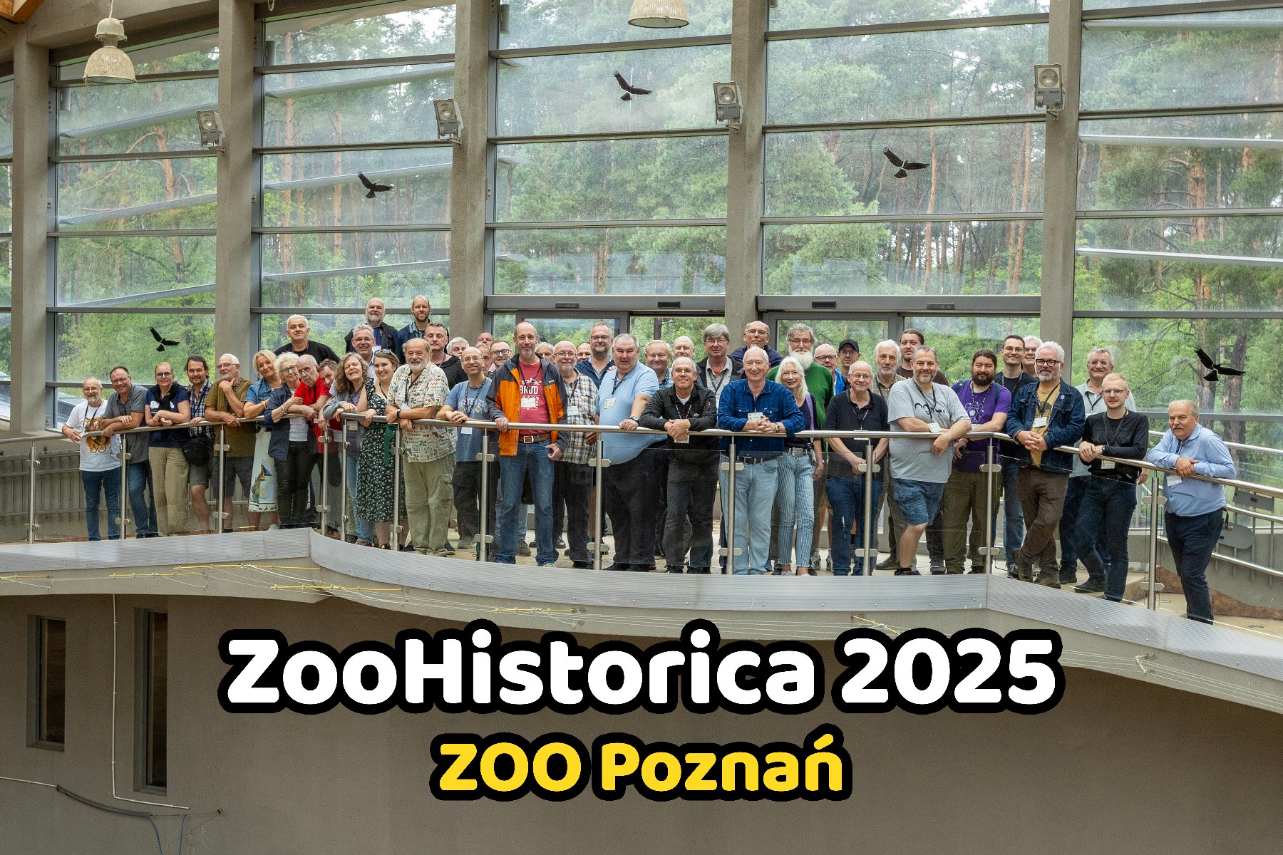 Grupowe zdjęcie ludzi na balkonie w oszklonym budynku.