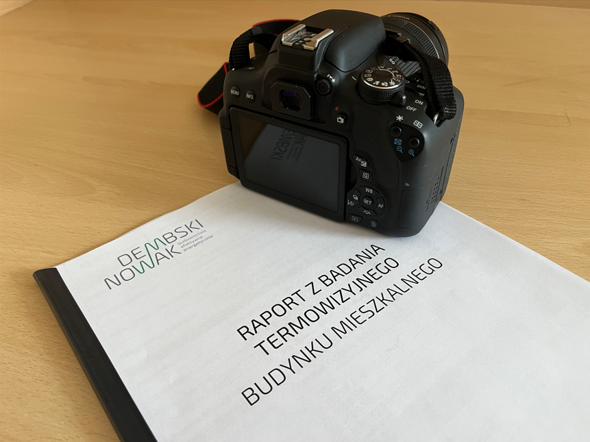 Ilustracja przedstawia dokoment z napisem "Raport z badania termowizyjnego budynku mieszkalnego" oraz kaparat fotograficzny.