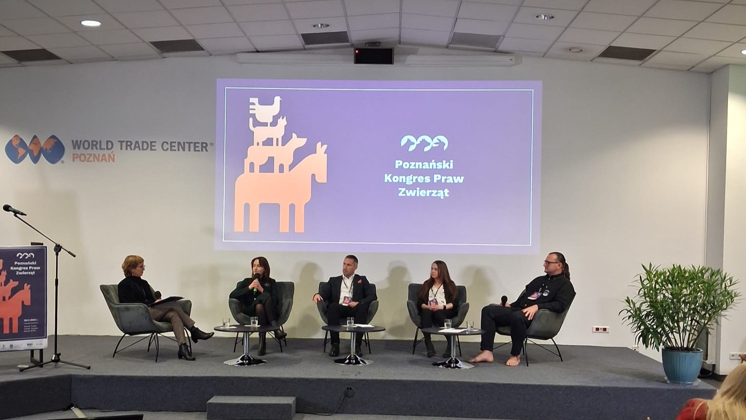 Ilustracja przedstawia panelistów kongresu dyskutujących na tle slajdu "Poznański Kongres Praw Zwierząt"