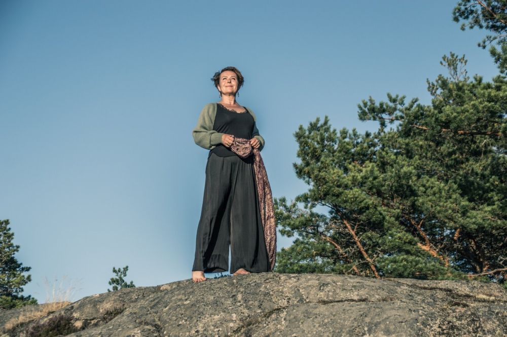 Jednorożec wygląda zza pokrytego mchem drzewa w lesie. Nastrój ilustracji jest mroczny, baśniowy.