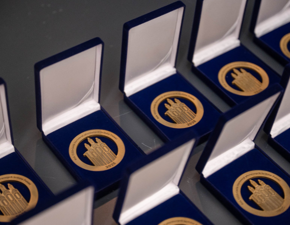 Kilka otwartych granatowych pudełek na aksamitnej wyściółce. W każdym pudełku znajduje się okrągły, złoty medal z symbolami Poznania oraz dużym napisem i datą w cudzysłowie: "1000 LAT" i "2025".