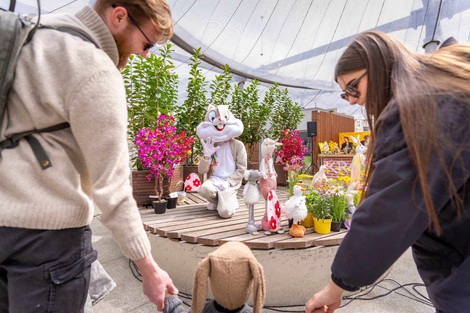 Kobieta i mężczyzna trzymają za ręce małe dziecko. W tle widac postać zająca.