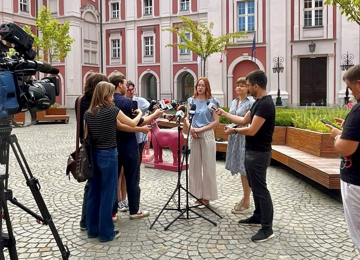 konferencja prasowa na dziedzińcu urzędu miasta, osoby stroją przed mikrofonem, przed nimi media z mikrofonami i kamerami